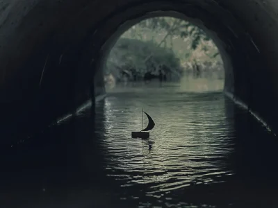 An image of a small, handcrafted boat floating in the water of a dark tunnel.