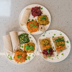 Photo of Ethiopian food on three white plates; including lentils and injera. 