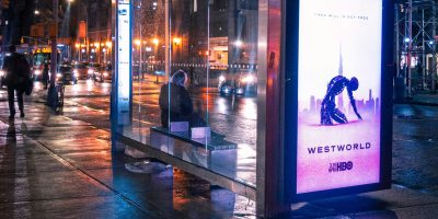 a person waits at a bus stop with a westworld advertisement