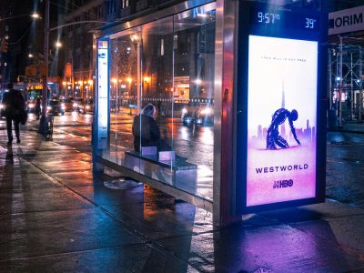 a person waits at a bus stop with a westworld advertisement
