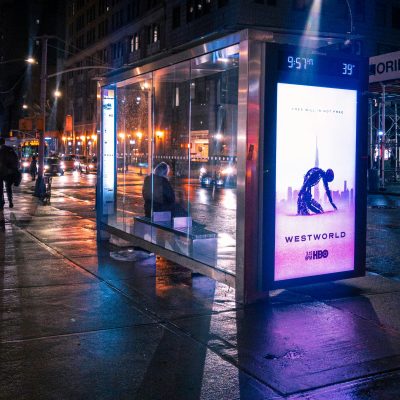 a person waits at a bus stop with a westworld advertisement
